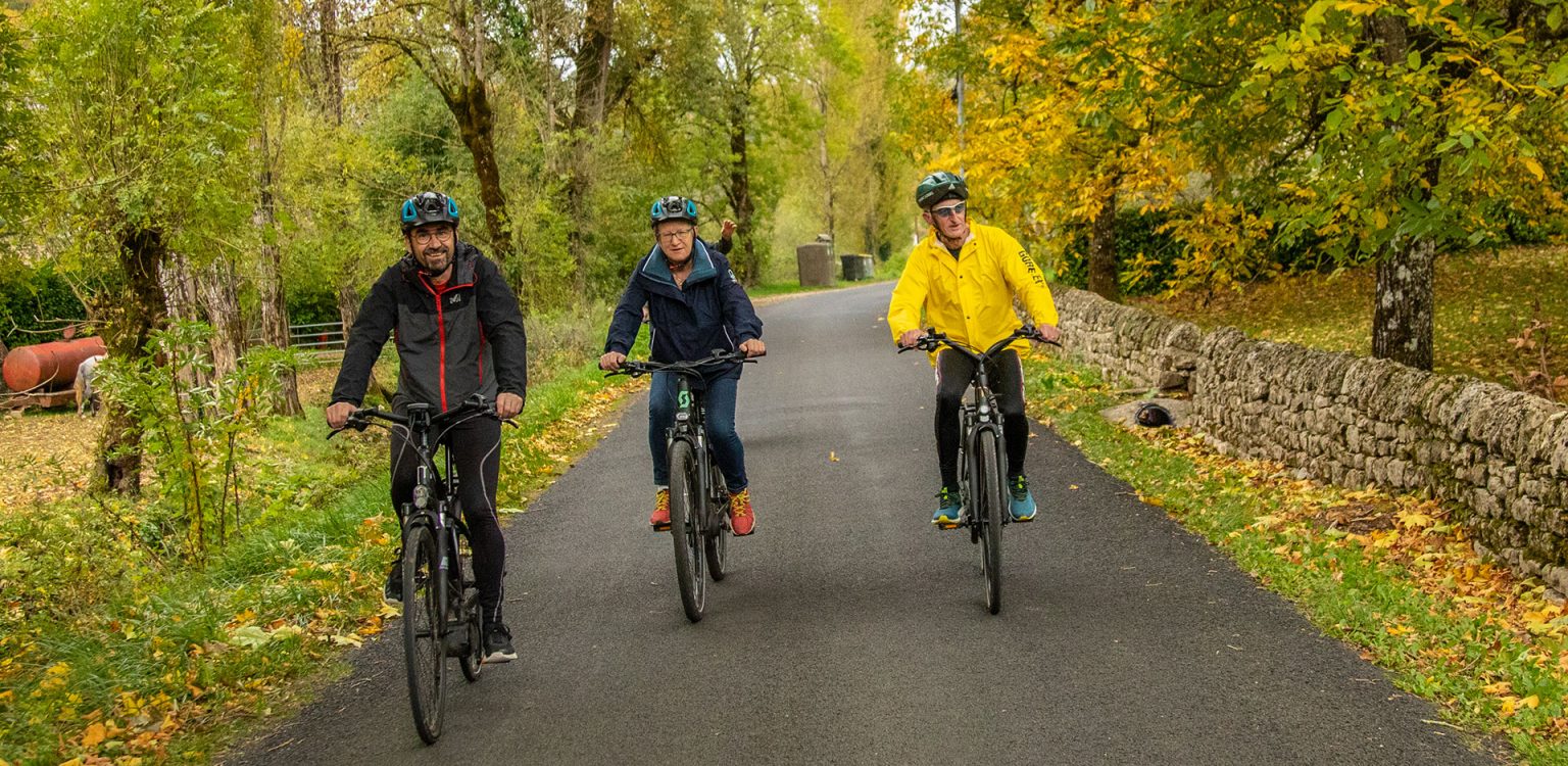 3 personnes en balade en vélo électrique sur un chemin tranquille au milieu des bois en automne en Aveyron